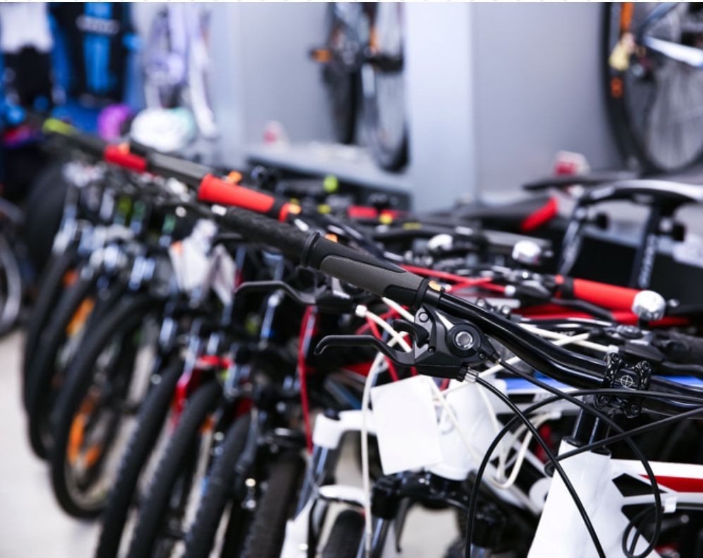 A row of various bicycles lined up in a bike shop, focused on handlebars and brakes.