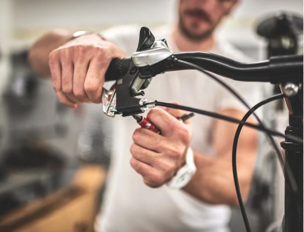 Person adjusting bicycle brake cables in a workshop setting.